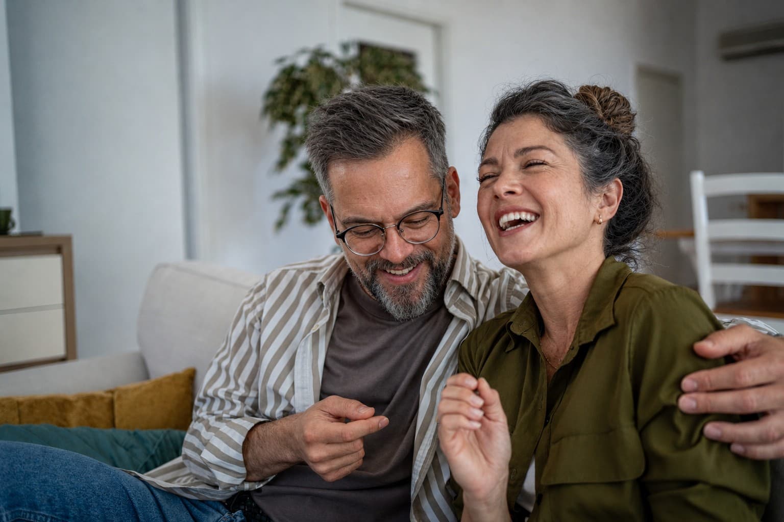 Una pareja de unos cincuenta años riendo en el sillón de su casa